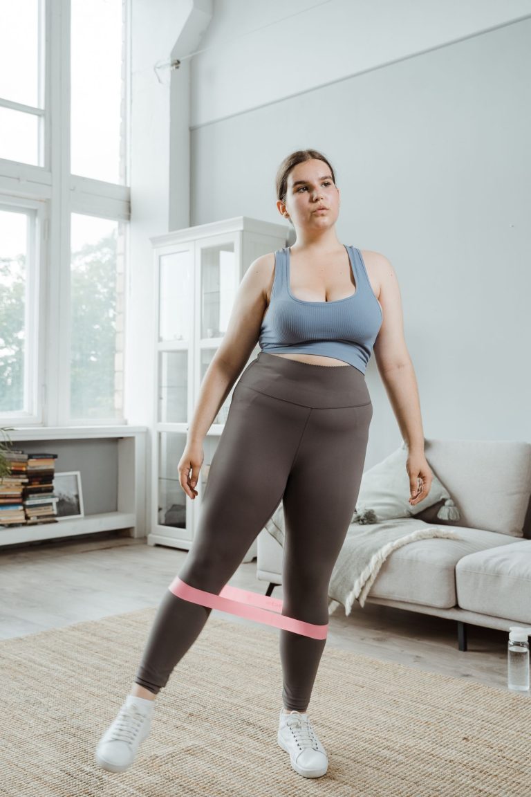 A woman exercising at home, pulling a resistance band apart with both hands